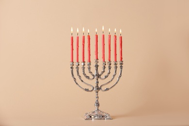 Silver menorah with burning candles on beige background. Hanukkah celebration