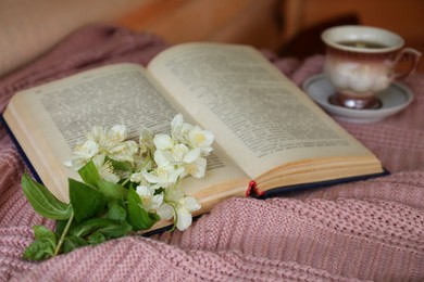 Beautiful jasmine flowers, open book and cup of aromatic drink on pink fabric