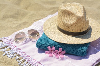 Photo of Stylish beach accessories and flowers on sand outdoors