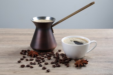 Photo of Metal turkish coffee pot, anise and cup of hot drink with beans on wooden table