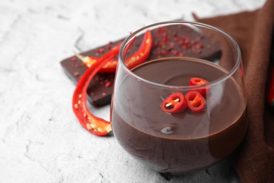 Photo of Glass of hot chocolate with chili pepper on white textured table, closeup. Space for text