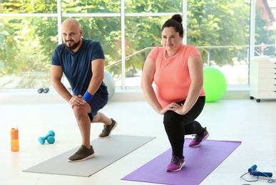 Overweight man and woman doing exercise on mats in gym