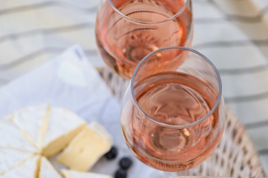 Photo of Glasses of delicious rose wine, food and basket on white picnic blanket, closeup