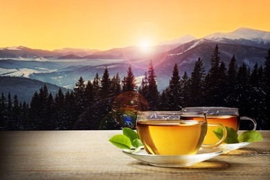 Cups of hot tea on wooden table and beautiful winter landscape on background