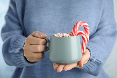 Woman holding cup of tasty cocoa with marshmallows and Christmas candy canes, closeup