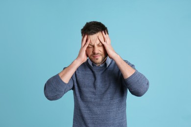 Man suffering from terrible migraine on light blue background