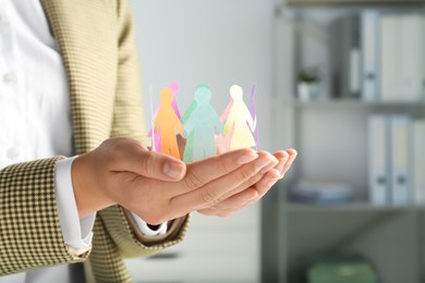 Woman holding paper human figures on blurred background, closeup. Diversity and inclusion concept