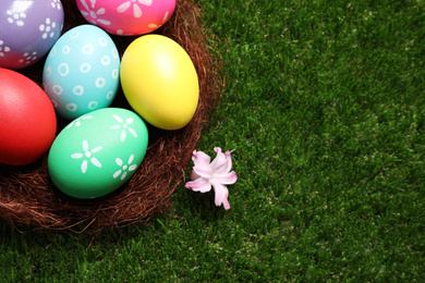 Colorful Easter eggs in decorative nest on green grass, closeup. Space for text