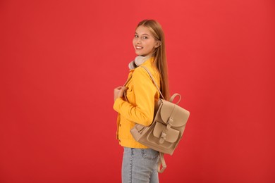 Teenage student with backpack and headphones on red background