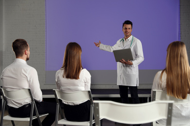Male doctor with laptop giving lecture in conference room with projection screen