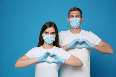 Volunteers in protective masks and gloves showing heart gestures on blue background. Aid during coronavirus quarantine