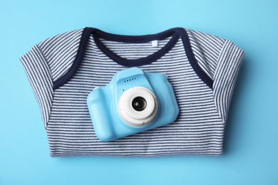 Toy camera and children's shirt on light blue background, top view. Future photographer