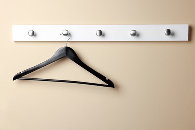 Photo of Rack with empty black clothes hanger on beige wall
