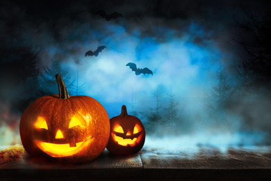 Scary Jack O Lantern pumpkins and flying bats in misty forest on Halloween. Space for text