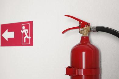 Fire extinguisher and emergency exit sign on white wall, closeup