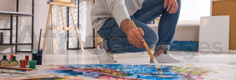 Young man painting on canvas with brush in artist studio. Banner design
