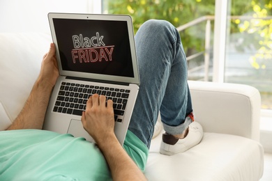 Man shopping online using laptop on couch at home, closeup. Black Friday Sale