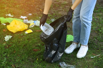 Woman with plastic bag collecting garbage on green grass, closeup