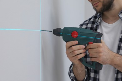 Man using cross line laser level for accurate measurement and drilling hole in light wall, closeup