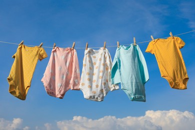 Clean baby onesies hanging on washing line against sky. Drying clothes