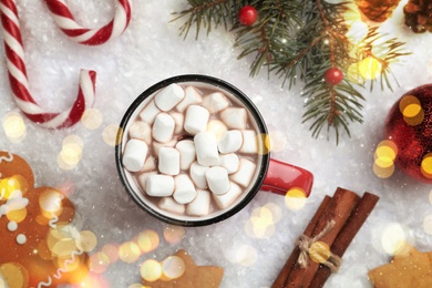 Hot drink with marshmallows, sweets and festive decor on snow, flat lay
