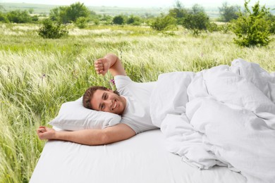 Happy man on bed with soft pillows and beautiful view of green meadow on background. Sleep well - stay healthy