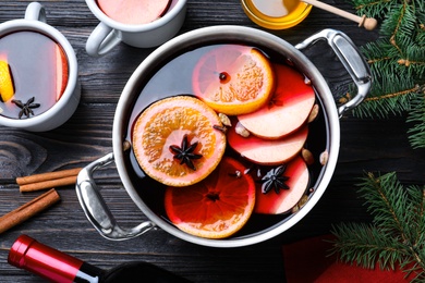 Delicious mulled wine and ingredients on black wooden table, flat lay