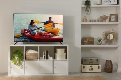 Modern TV set on wooden stand in room. Scene of adventure movie on screen