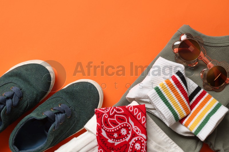 Stylish child clothes, shoes and accessories on orange background, flat lay. Space for text