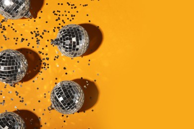 Bright shiny disco balls and confetti on orange background, flat lay. Space for text