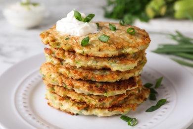 Delicious zucchini fritters with sour cream and green onion on plate, closeup