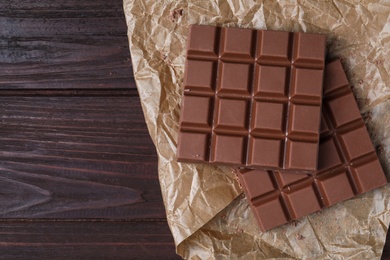 Photo of Tasty milk chocolate bars on wooden table, flat lay. Space for text