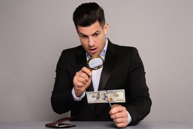 Photo of Expert authenticating 100 dollar banknote with magnifying glass at table on light grey background. Fake money concept