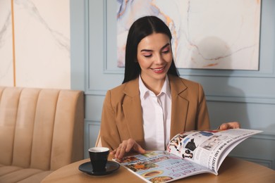 Woman with cup of coffee reading magazine at cafe in morning