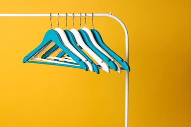 Bright clothes hangers on metal rack against yellow background