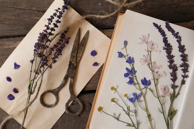 Old scissors with beautiful dried flowers and book on wooden table, flat lay