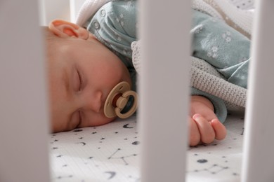 Adorable baby with pacifier peacefully sleeping in crib