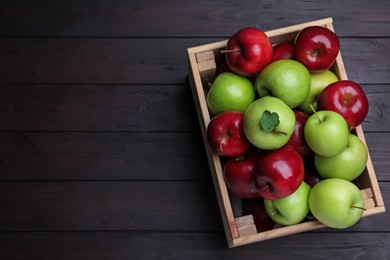 Fresh ripe red and green apples in wooden crate on black table, top view. Space for text