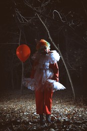 Terrifying clown with red air balloon outdoors at night. Halloween party costume