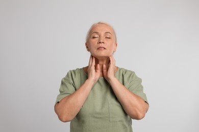 Mature woman doing thyroid self examination on light grey background