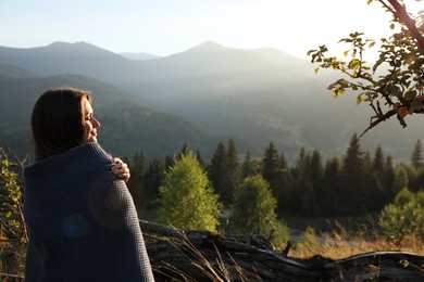 Photo of Woman with cozy plaid enjoying warm sunlight in mountains