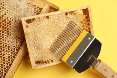 Photo of Hive frames with honeycombs and uncapping fork on yellow background, flat lay. Beekeeping