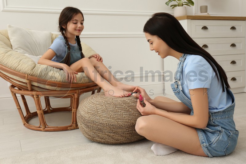 Young mother applying polish on daughter's nails at home
