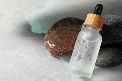 Bottle of face serum and spa stones on wet grey marble table, closeup. Space for text