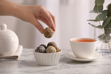 Woman taking delicious vegan candy ball at white marble table indoors, closeup