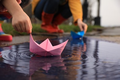 Little girl and her mother playing with paper boats near puddle outdoors, closeup