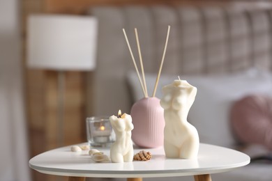 Photo of Beautiful body shaped candles, seashells and air reed freshener on table indoors