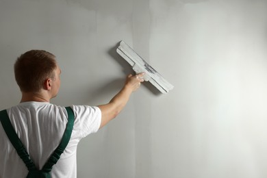 Professional worker plastering wall with putty knife. Space for text