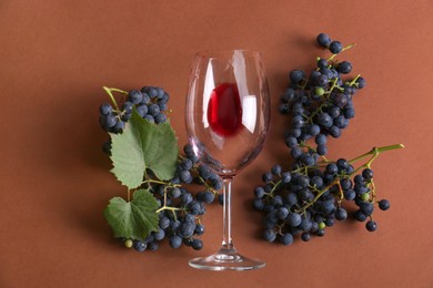 Overturned glass with red wine and grapes on brown background, flat lay