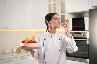 Happy professional confectioner with cake showing delicious gesture in kitchen